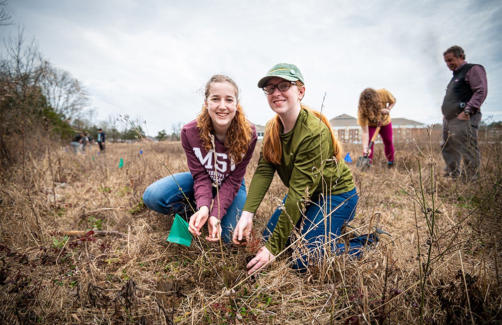 Emma Squires (left), sophomore forestry major, and Amelia Horner (right), junior wildlife, fisheries and aquaculture major, plant cedar trees by the College View apartments 