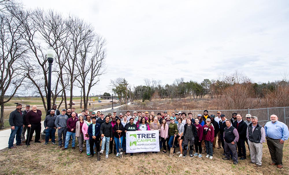 A large crowd of 多多直播 students, faculty and staff with a Tree Campus USA banner at the Arbor Day celebration